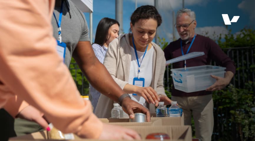 Volunteers working together at an outdoor event, sorting donations and packing food items in boxes for a charitable cause.